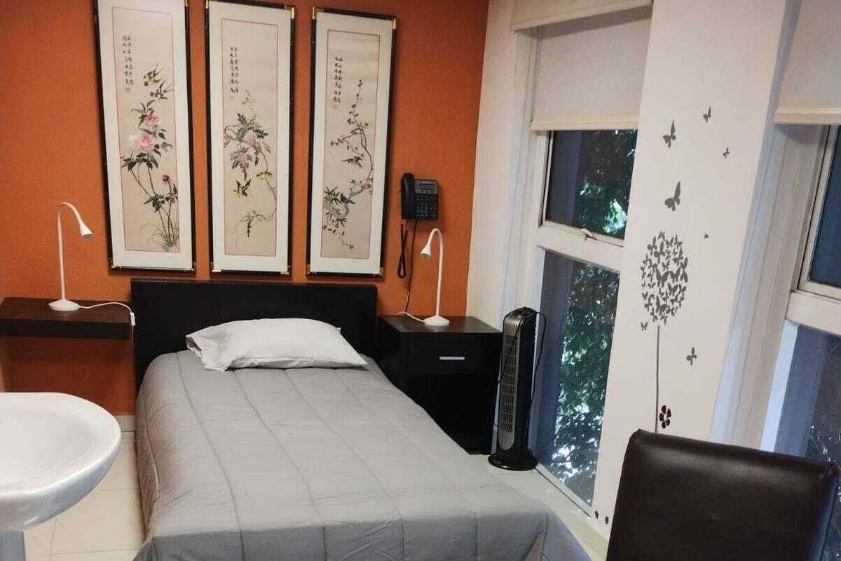 A bedroom with a bed, bedside tables, a chair, a small table, and artwork on the wall.