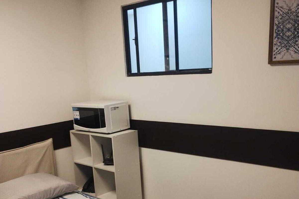 A bedroom with a bed, a microwave, a shelf, a window, and a wall art piece.