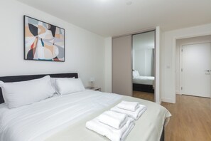 Una camera d'albergo moderna con un letto rifatto, un comodino con una lampada e un grande quadro astratto appeso al muro.