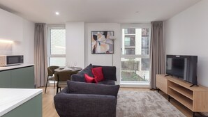 A modern living room with a grey sofa, a flat-screen TV, and a dining area with a table and chairs. - Terrace House in Bristol (Bristol)