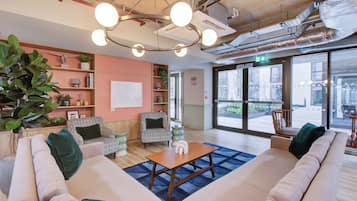 A spacious lobby with a large sofa, patterned chairs, a wooden coffee table, and a large window offering a view of the street.