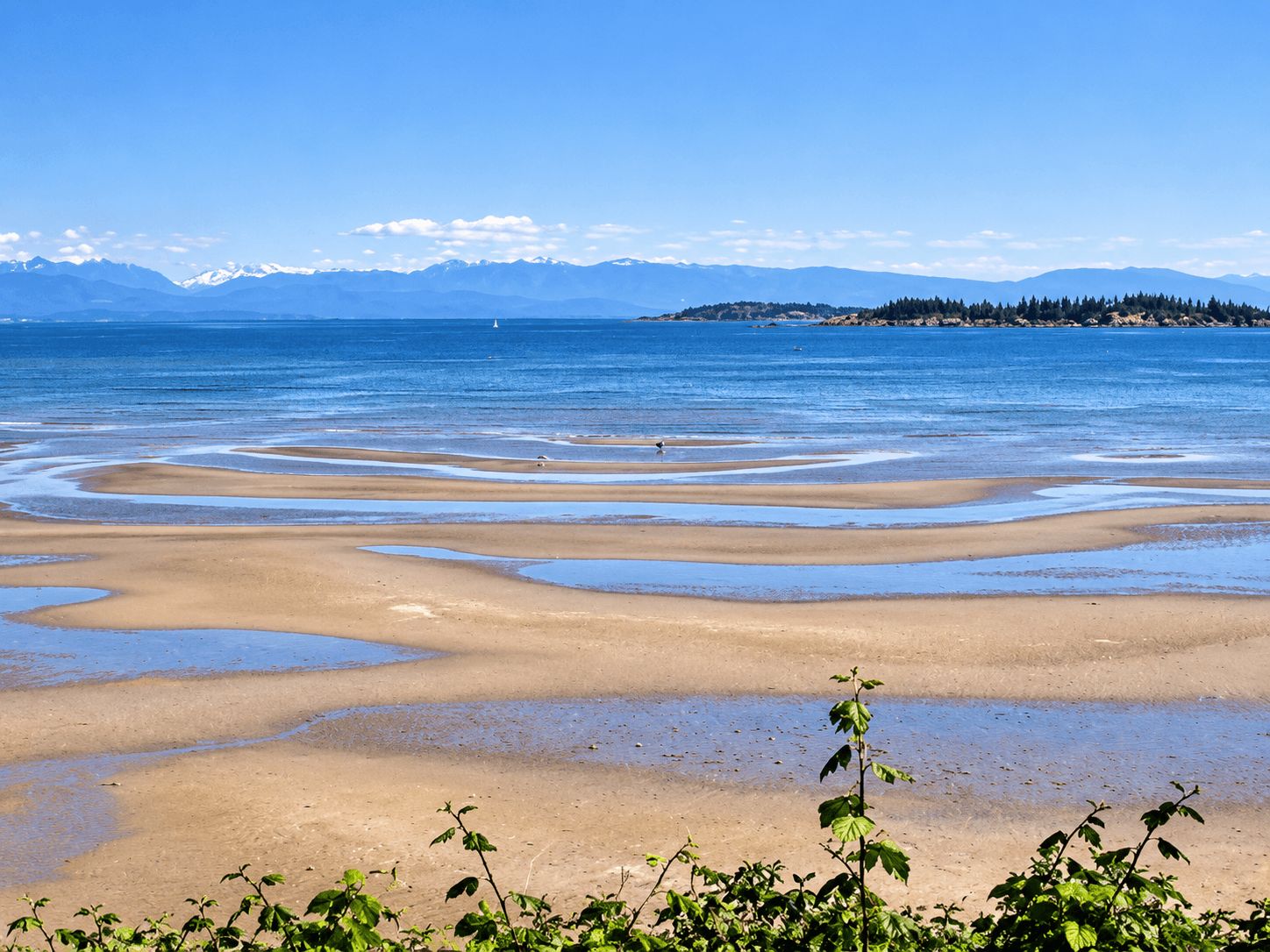 Une plage avec une eau d’un bleu limpide et des montagnes qui se dessinent à l’horizon.