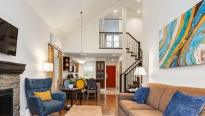 A spacious living room with a fireplace, a dining area, and a staircase leading to an upper level. - Beach Daze! Peaceful Retreat Near Rathtrevor Beaches (Parksville)