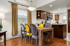 A dining area with a wooden table and chairs, a kitchen with wooden cabinets and a microwave, and a window with curtains.