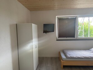 A bedroom with a bed, a wall-mounted TV, and a window with blinds.