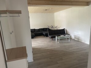 A modern living room with a sectional sofa, a glass coffee table, and a wooden ceiling.