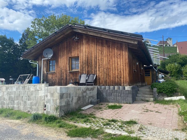 A wooden cabin with a satellite dish, a small porch, and a brick pathway leading to the entrance.