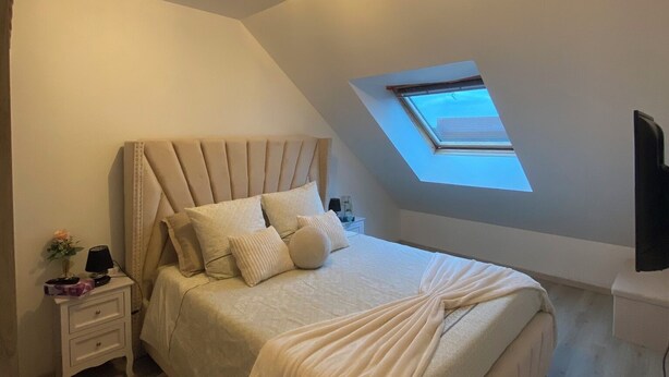 Ein Schlafzimmer mit einem großen Bett, einem Nachttisch, einem Fernseher und einem Oberlicht.