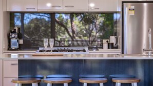 Une cuisine moderne dotée d’une grande fenêtre, d’un réfrigérateur en acier inoxydable et de quatre tabourets en bois.