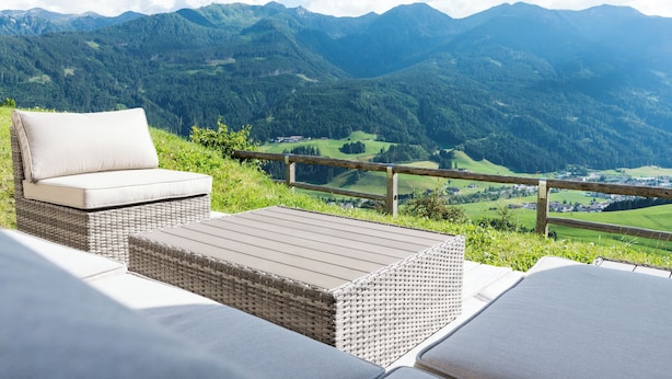 Ein Sitzbereich aus Rattan im Freien mit Kissen, mit Blick auf eine gebirgige Landschaft.
