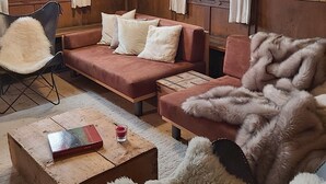 Ein gemütlicher Raum mit Holzbalkendecke, zwei Sofas, einem flauschigen Sessel und einem kleinen Tisch mit einem Buch und einem Glas.