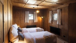 Ein Holzhütten-Zimmer mit zwei Betten, einem Heizkörper und zwei mit Vorhängen versehenen Fenstern.
