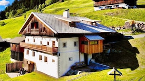 Ein traditionelles Chalet mit geneigtem Dach, Holzbalkonen und einer kleinen Terrassenfläche.