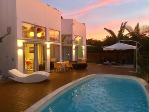Une maison moderne dotée d’une piscine, d’un espace salon extérieur et d’un patio couvert.