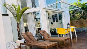 A modern outdoor patio with wooden lounge chairs, a glass enclosure, and a yellow table. - No1 Stylish Beach House With Pool (Florianópolis)