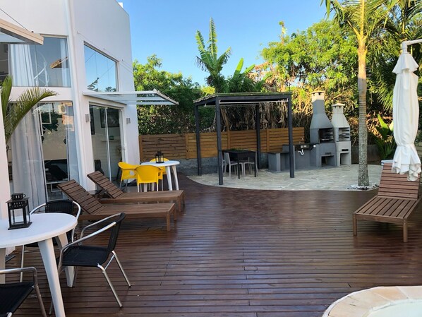 Une terrasse avec un revêtement de sol en bois, des sièges d’extérieur et un espace barbecue.