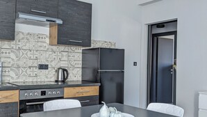 Una cocina moderna con armarios oscuros, un refrigerador negro y un respingo de azulejos. Hay una mesa de comedor con cuatro sillas blancas y un plato de adornos.