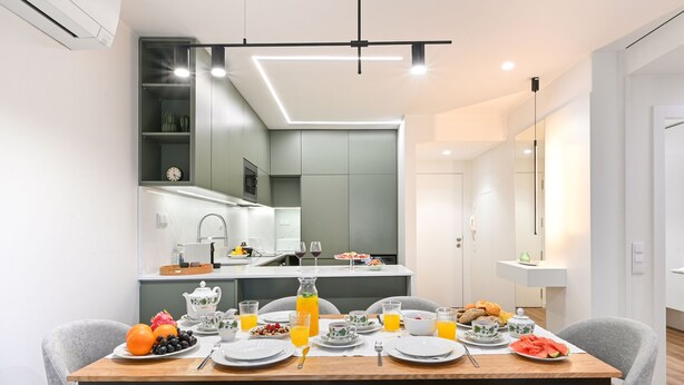 A modern dining area with a wooden table set for breakfast, a kitchen in the background, and a large mirror reflecting the space. - ON Apartments - Matosinhos Premium  (Matosinhos)