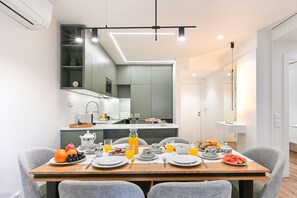 Un espace repas moderne avec une table en bois dressée pour le petit-déjeuner, une cuisine en arrière-plan et un grand miroir qui reflète l’ensemble de la pièce.