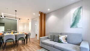 A modern living room with a grey sofa, a dining table with chairs, and a kitchen area in the background. - ON Apartments - Matosinhos Premium  (Matosinhos)