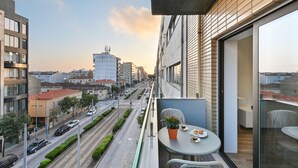A balcony with a table and chairs, overlooking a city street with buildings and a train track. - ON Apartments - Matosinhos Premium  (Matosinhos)