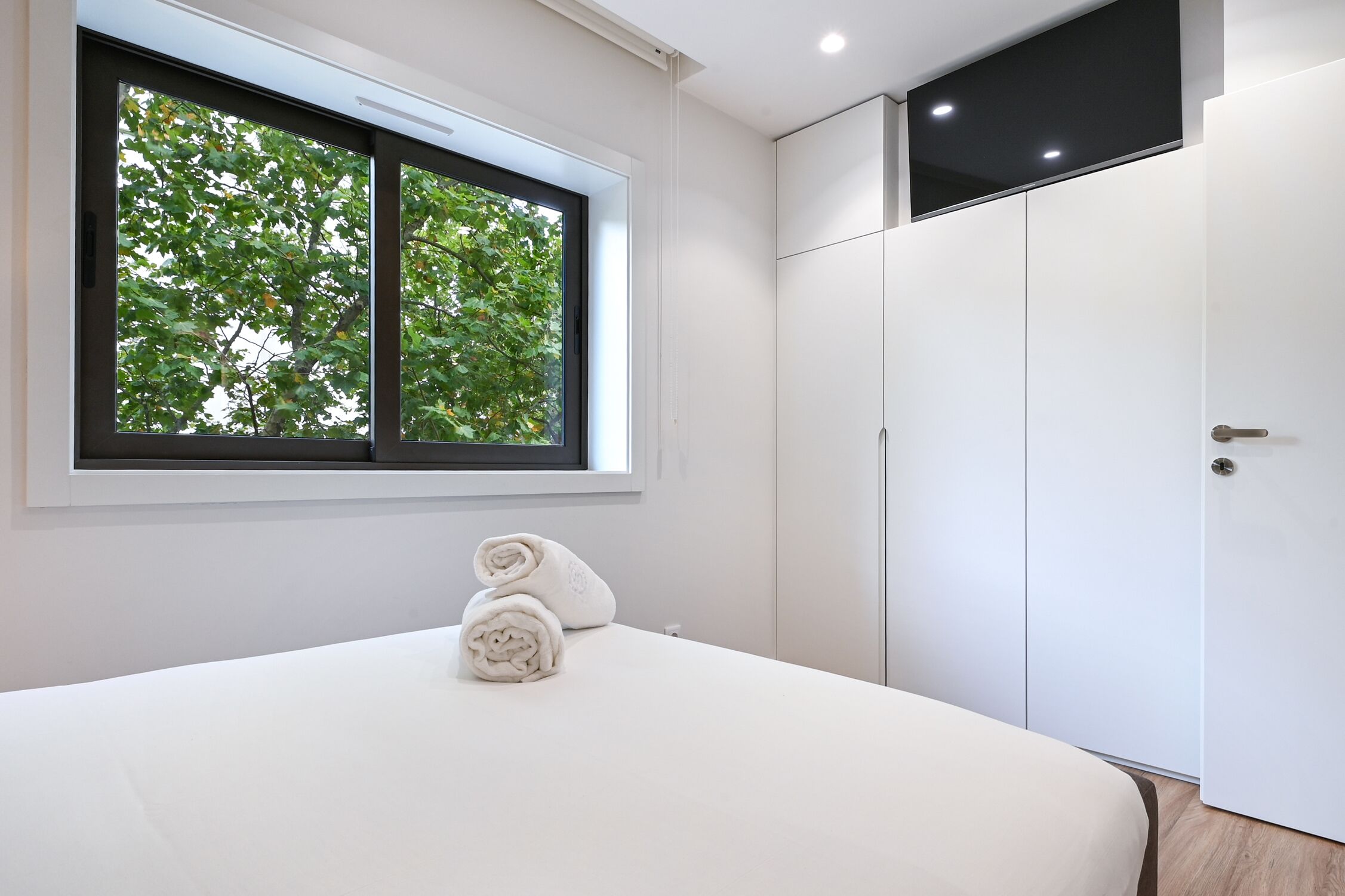 A bedroom with a bed, a window with a view of trees, and a wardrobe.