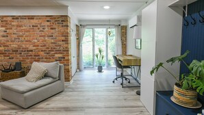 Moderni huone, jossa on tiiliseinä, sohva, työpöytä ja ruukussa oleva kasvi.