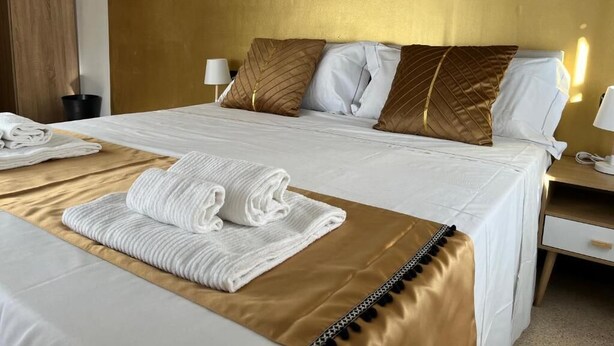 A hotel room with a large bed, a bedside table with a lamp, and neatly folded towels on the bed. - Genova Gold Rooms (Genoa)