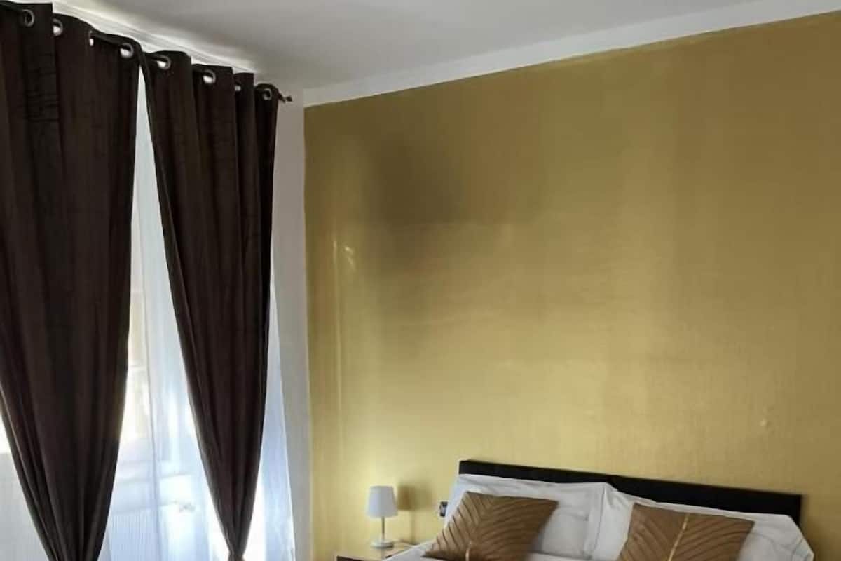 A hotel room with a large bed, wooden headboard, and a gold accent wall.