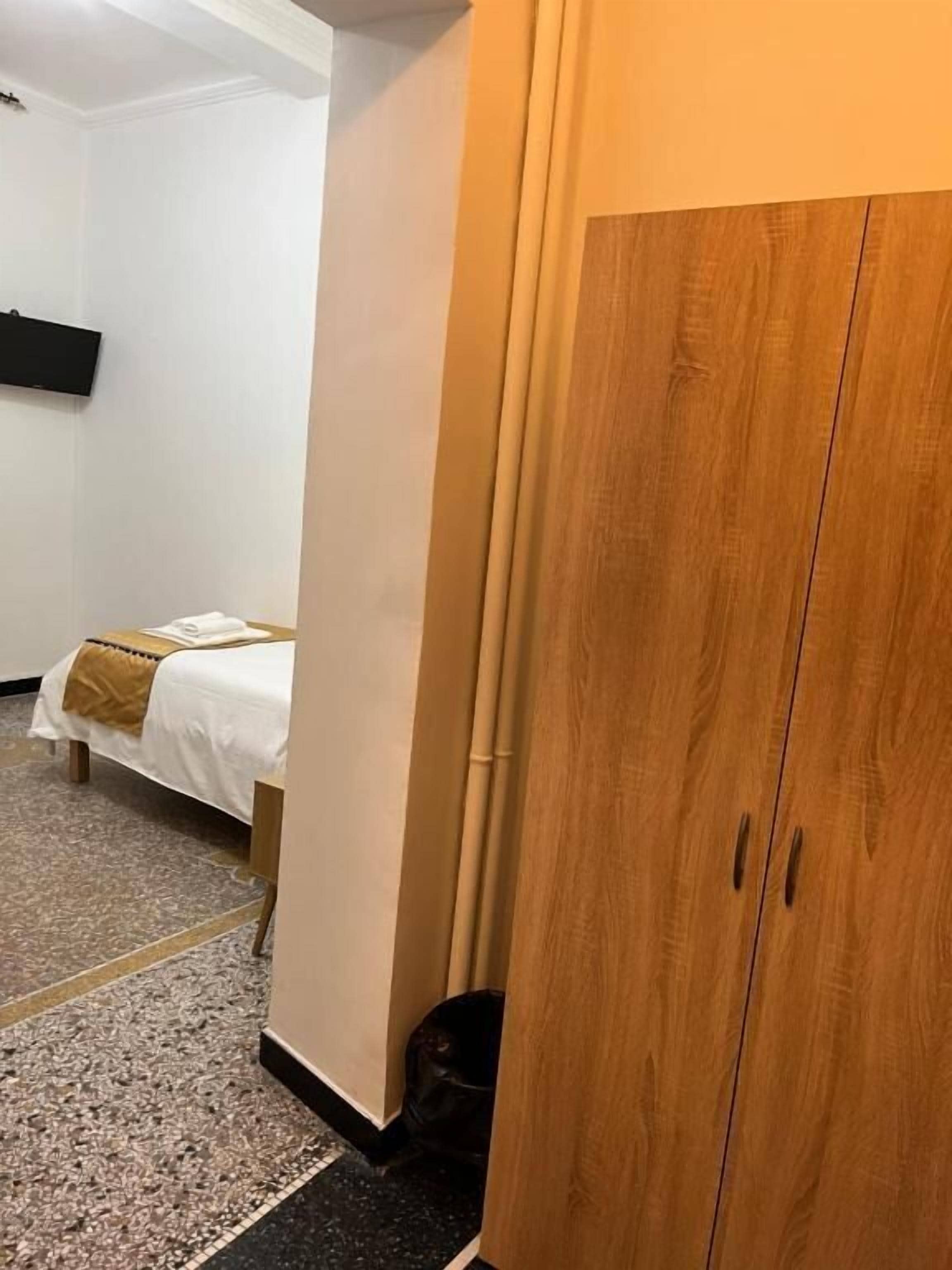 Quarto de hotel com cama, guarda-roupa e lixeira.