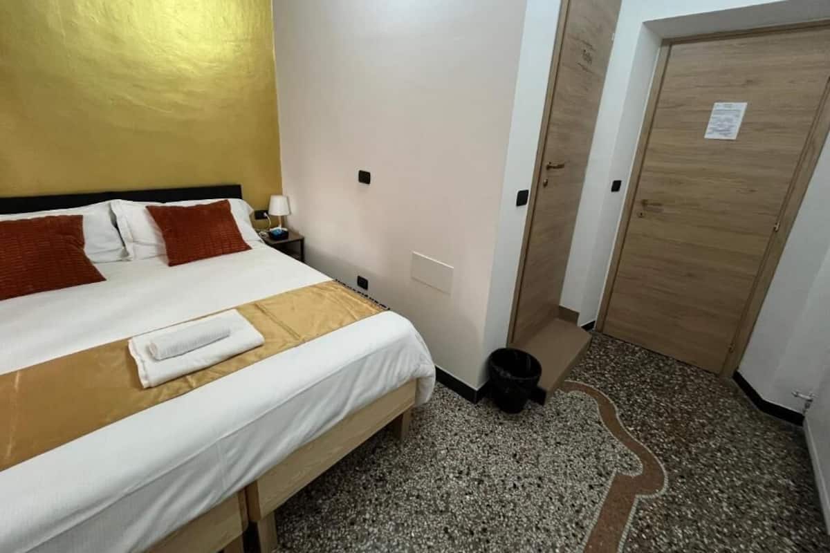 A hotel room with a bed, a nightstand, a wooden door, and a carpeted floor.