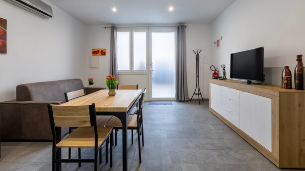 Een moderne woonkamer met een bank, eettafel, televisie en een groot raam.