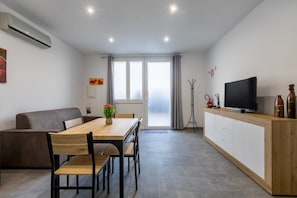 Uma sala de estar moderna com sofá, mesa de jantar, televisão e uma grande janela.