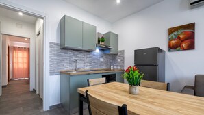 Een moderne keuken met een houten eettafel, grijze kastjes en een schilderij van fruit aan de muur.