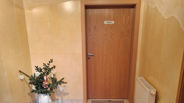 A hallway with a tiled floor, a wooden door labeled "PRIVATE," and a potted plant with flowers. - Vacation apartment Am Ranis (Oederan)