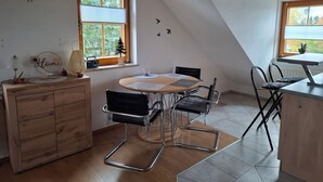 A cozy kitchen with a wooden ceiling, a round table with chairs, and a window with blinds. - Vacation apartment Am Ranis (Oederan)