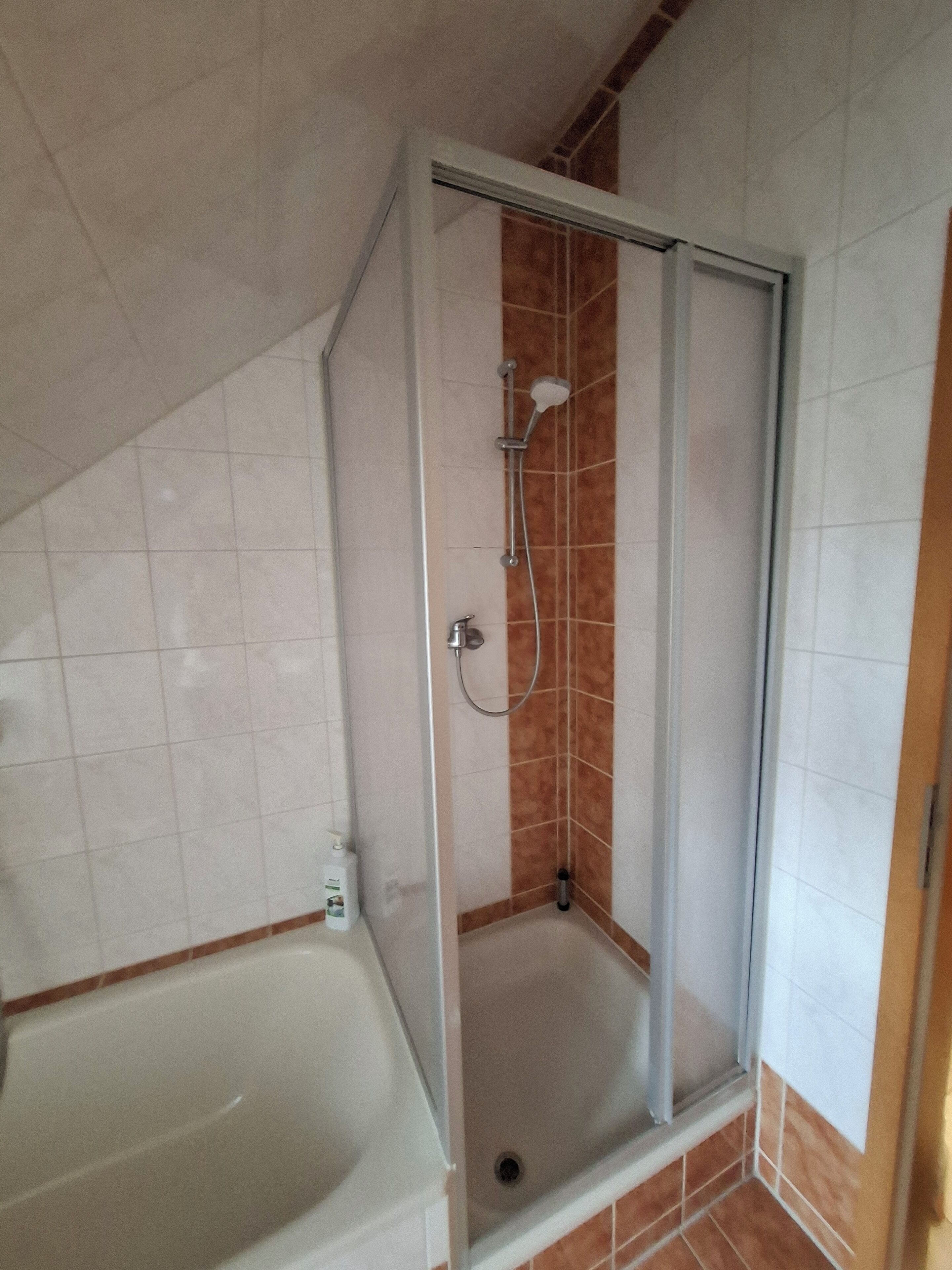 Eine Dusche mit Glastür, eine weiße Badewanne und ein Eckfliesendesign.