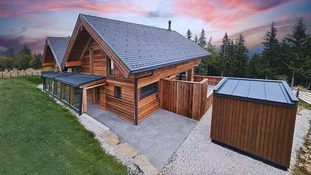 Una cabaña moderna de madera con techo inclinado, un porche cubierto y un cobertizo pequeño.