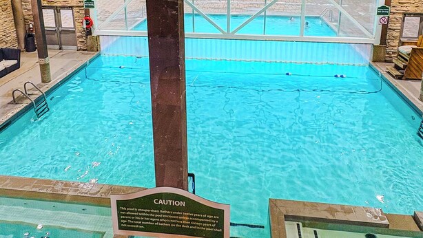Una piscina interior con agua cristalina, una torre de salvavidas y un letrero de precaución.