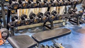 Un gimnasio con diversos equipos, incluyendo mancuernas, una banca y una cinta de correr.