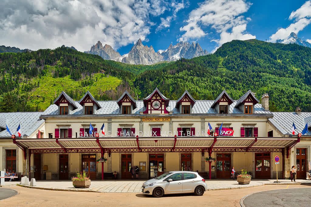 A hotel with a traditional European architectural style, featuring a prominent signboard and a view of mountains in the background.