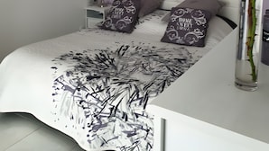 Een moderne slaapkamer met een bed, nachtkastje, lamp en een vaas met een roos.