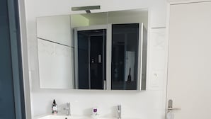 Een moderne badkamer met een witte wastafel, twee wasbakken, een grote spiegel en een paars handdoekrek.