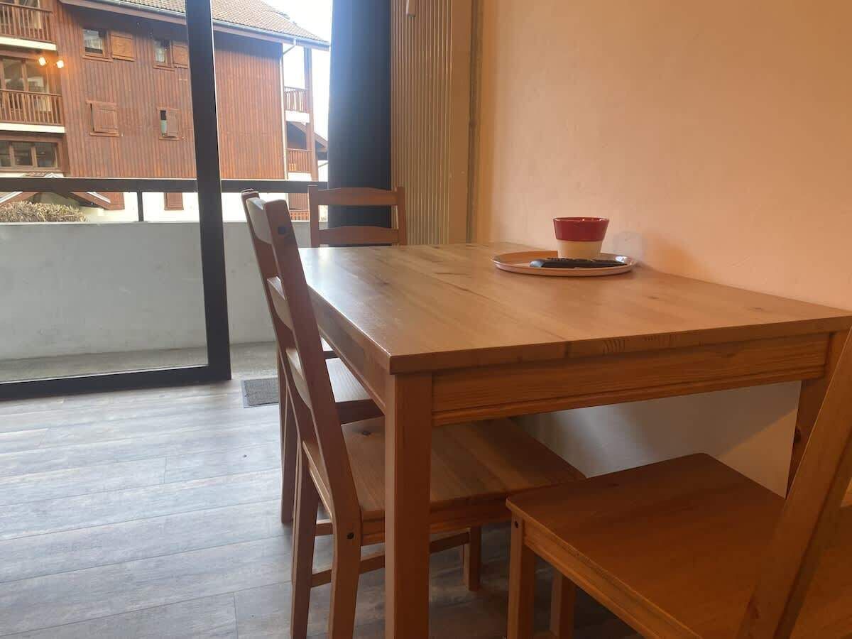 A wooden dining table with chairs, a bowl, and a plate on a balcony with a view of a building.