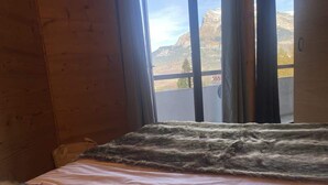 A room with a bed, a window with a view of mountains, and a wooden wall. - Avalon Central 1 Bed Apartment by Tram Station (Saint-Gervais-les-Bains)