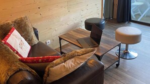 A cozy room with a leather sofa, a laptop on a wooden table, a TV mounted on the wall, and a view of the outdoors through a glass door. - Avalon Central 1 Bed Apartment by Tram Station (Saint-Gervais-les-Bains)