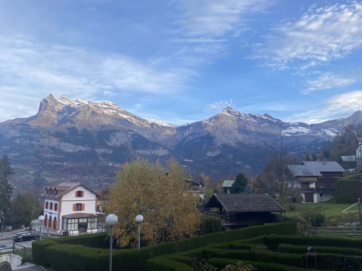 A mountain village with traditional houses, a church, and a clear view of snow-capped peaks.