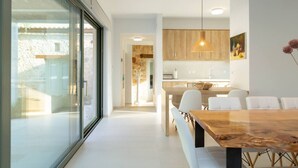 Een moderne keuken met houten kastjes, een eethoek met een marmeren tafel, en een grote schuifdeur naar een buitenruimte.