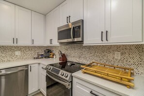 A kitchen with white cabinets, a microwave, a stove, and a coffee maker. - The Rockledge Billiard House (Rockledge)