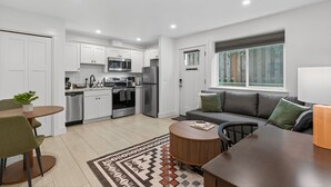 A modern kitchen with white cabinets, stainless steel appliances, and a dining area with a round table and chairs. - St. Johns Nest, Near Cathedral Park (Portland)